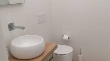 Un baño moderno con un mueble de tocador de madera, un lavabo blanco, un inodoro y un dispensador de papel higiénico.