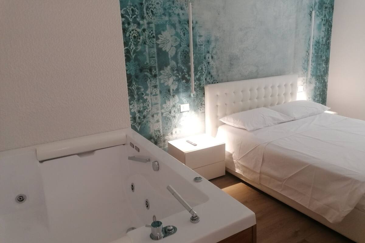 A bedroom with a white bed, a nightstand, and a white bathtub.
