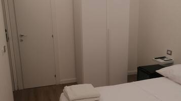 A bedroom with a bed, a wardrobe, an air conditioning unit, a bedside table with a phone, and a nightstand.