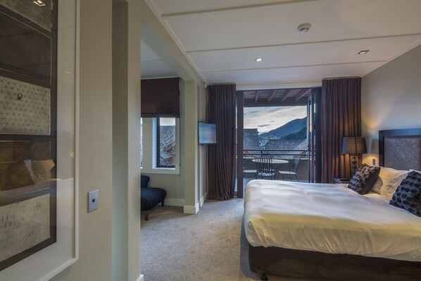 A hotel room with a large bed, a TV, a balcony with a view of mountains, and a framed artwork on the wall. - Karamata (Queenstown)