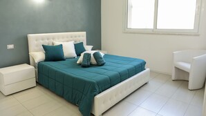 A bedroom with a large bed, a nightstand, a chair, and a window. - The Smerald (Alghero)