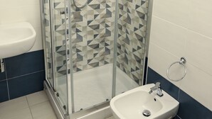 A bathroom with a glass-enclosed shower, a white sink, and a bidet. - The Smerald (Alghero)