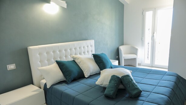 A bedroom with a large bed, a nightstand, and a chair. - The Smerald (Alghero)