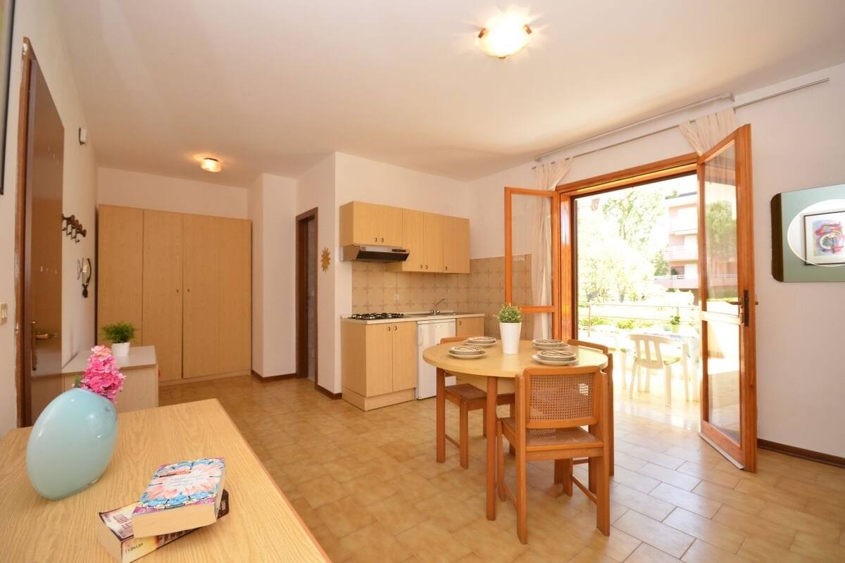 Cocina compacta con armarios de madera, una mesa de comedor con sillas y un gran ventanal corredero que da a un espacio exterior.