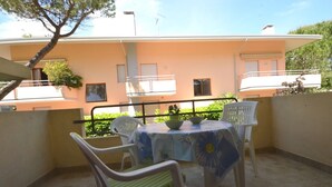 A balcony with a table and chairs, a peach-colored building in the background, and a tree. - Appartamenti dei Fiori (Lignano Sabbiadoro)