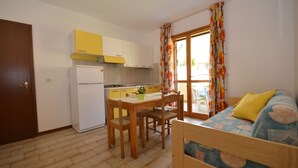A compact kitchen with a dining table, chairs, and a refrigerator. - Appartamenti dei Fiori (Lignano Sabbiadoro)