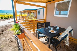 A wooden deck with a table and chairs, a bench, and potted plants.