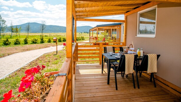 Eine Holzterrasse mit Tisch und Stühlen, einem Fenster und Blick auf eine Berglandschaft.