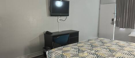 Une chambre d’hôtel comprenant un lit, un bureau, une chaise, un téléviseur fixé au mur et une porte avec des rideaux.