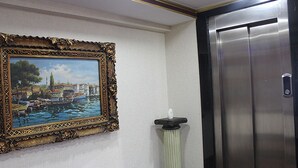Ein gerahmtes Gemälde zeigt einen Hafen, einen modernen Aufzug und eine hohe, schlanke Vase auf einem Sockel.