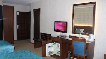 Hotelkamer met een bed, een bureau met een computer, een kleine koelkast, een spiegel en een deur.