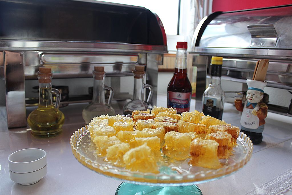 Une table de buffet avec un plat en verre rempli de pâtisseries en forme de nid d’abeilles, une bouteille de sauce et une petite figurine.