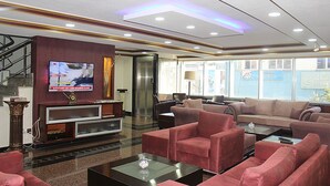 Eine moderne Lobby mit Flachbildfernseher, bequemen Sitzgelegenheiten, einer Rezeption und einer Treppe.