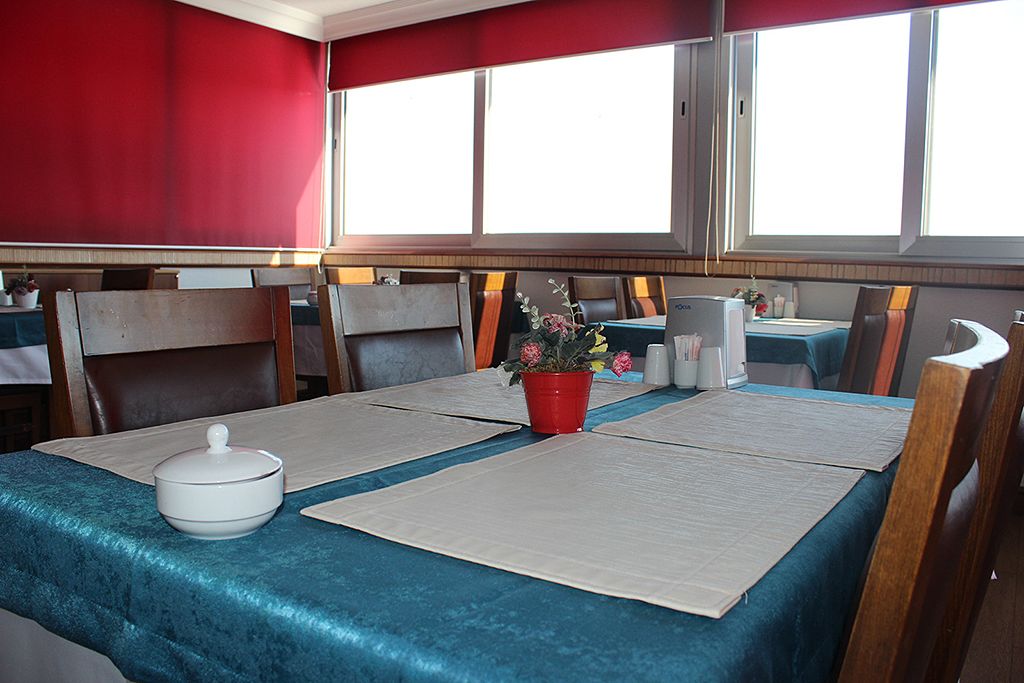 A dining area with tables set for two, a red wall, and a window providing natural light.