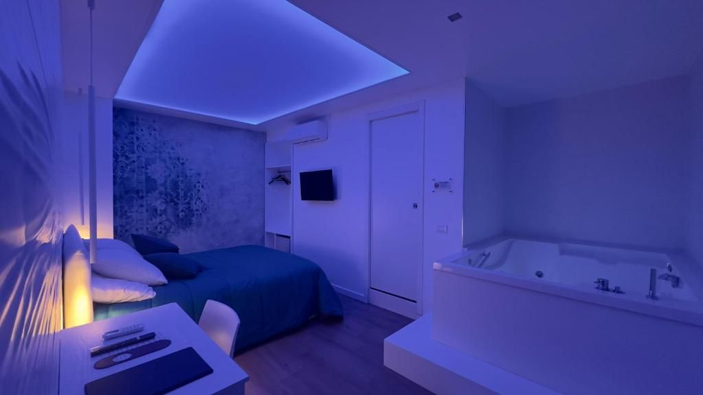 Ein modernes Schlafzimmer mit einem Bett, einem Nachttisch mit Fernbedienung, einem an der Wand befestigten Fernseher und einer großen Badewanne.