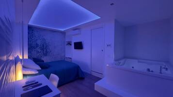Ein modernes Schlafzimmer mit einem Bett, einem Nachttisch mit Fernbedienung, einem an der Wand befestigten Fernseher und einer großen Badewanne.