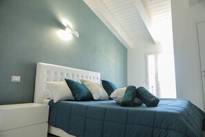 Un dormitorio con una tapizada blanca, ropa de cama color aguamarina y una ventana que deja entrar luz natural.