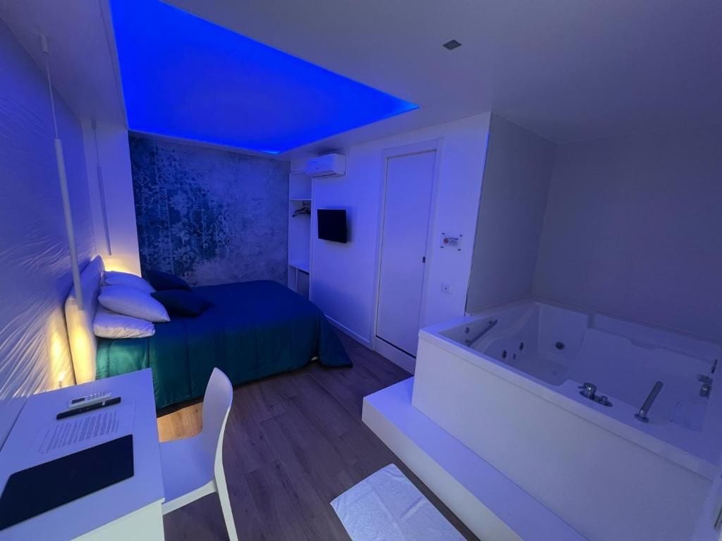 Une chambre à coucher avec un lit, un bureau avec des papiers, un téléviseur fixé au mur et une baignoire.