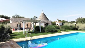 Une piscine à l’eau d’un bleu limpide, entourée d’un jardin et agrémentée d’un kiosque blanc.