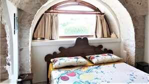 Une chambre à coucher avec un lit placé sous une fenêtre en arc de pierre, une tête de lit en bois et une couvre-lit à motifs.