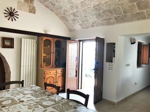 Ein Zimmer mit Esstisch, Stühlen, einem Holzschrank und einer Tür zu einem Außenbereich.