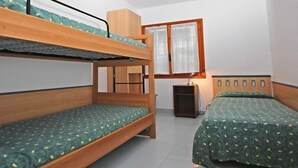 Una habitación con literas, una mesita y una ventana con cortinas.