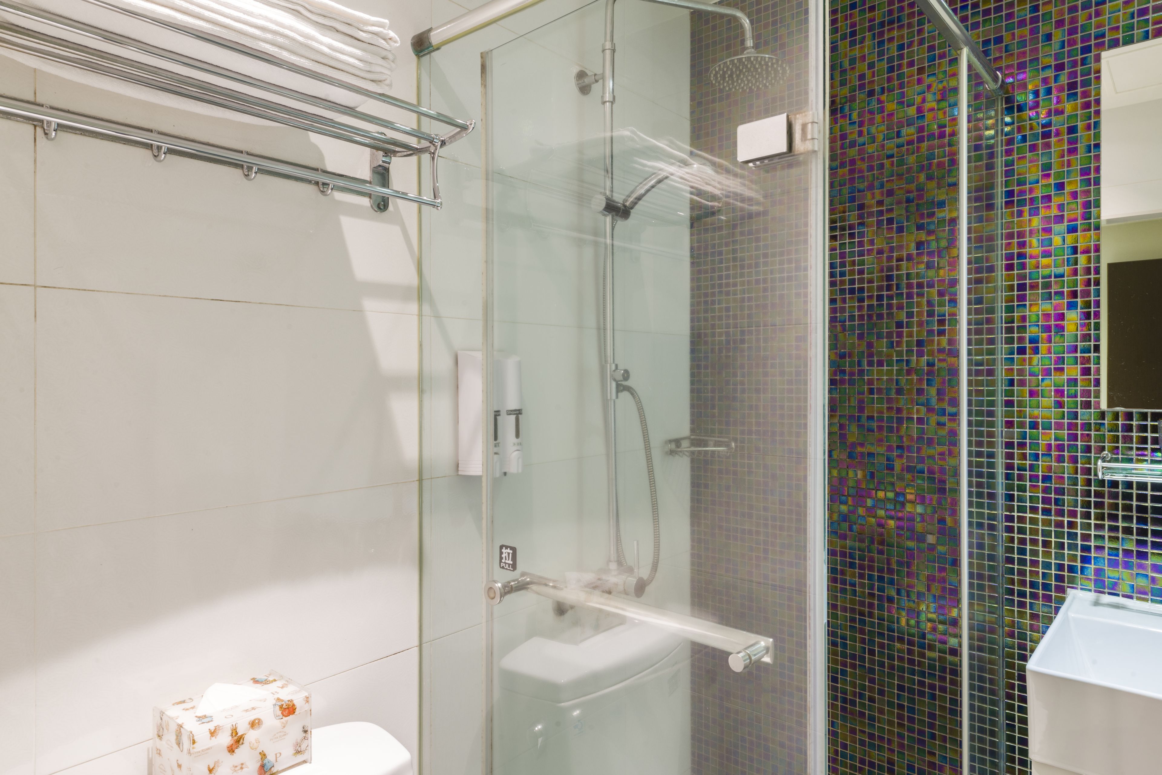 Un bagno moderno con doccia vetrata, parete rivestita di piastrelle con motivo a mosaico colorato e lavandino bianco.