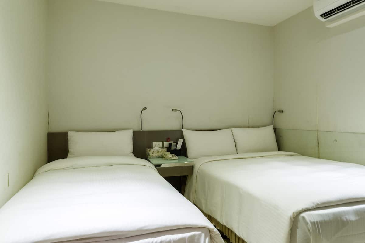 A hotel room with two single beds, a bedside table with a lamp, and an air conditioning unit on the wall.