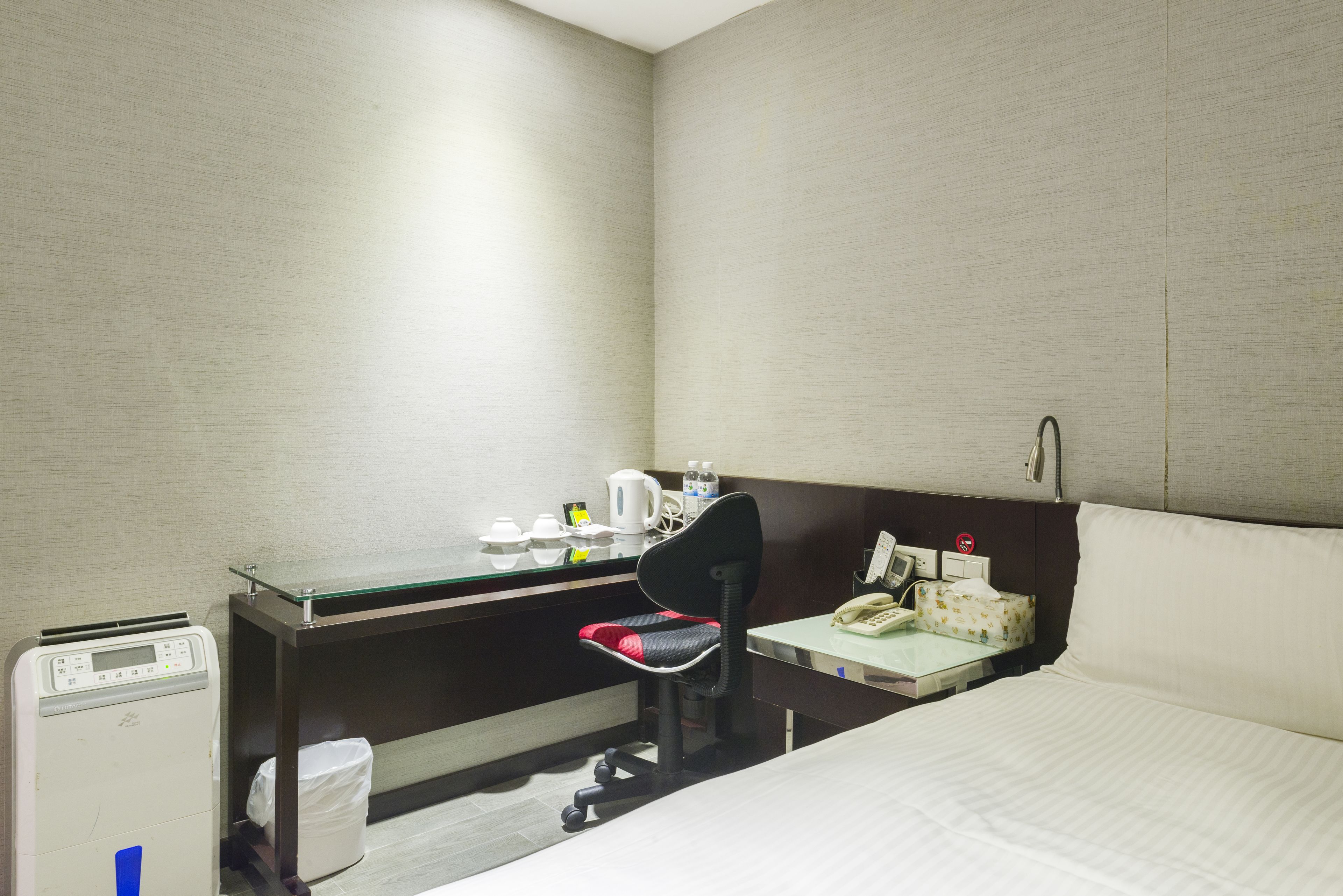 A hotel room with a desk, chair, bed, and a small table with a telephone and a tissue box.