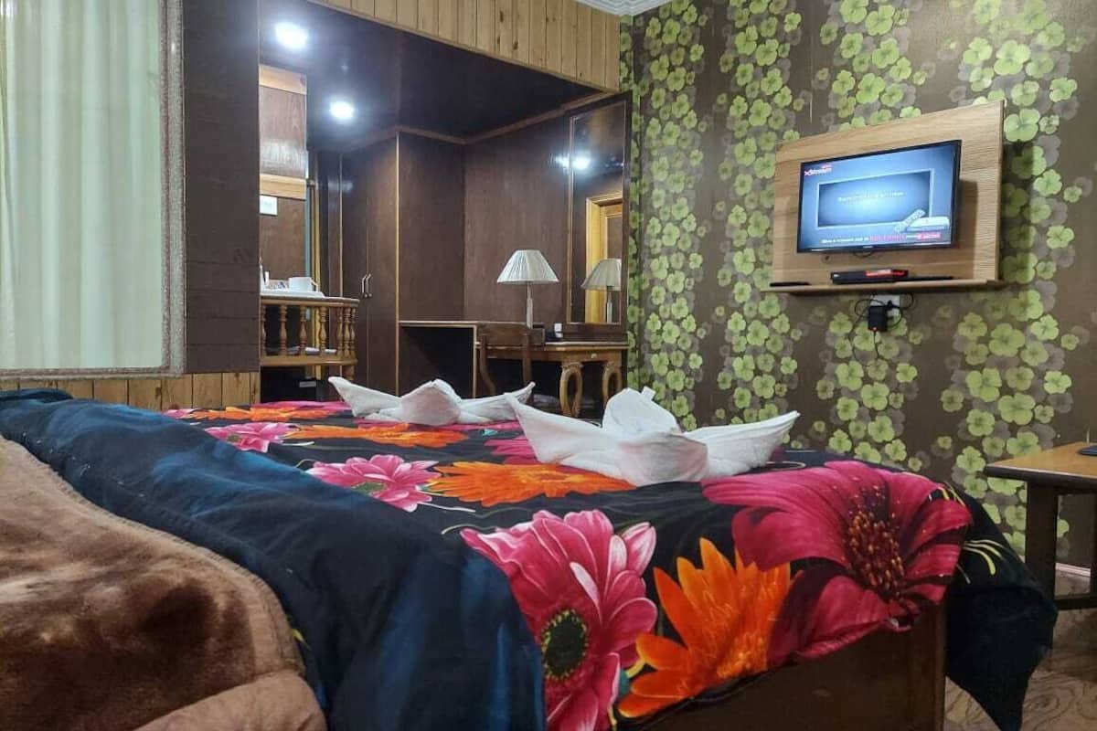 Quarto de hotel com cama, televisão na parede, escrivaninha e espelho.