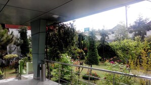 Entrada de hotel con piso de mármol, baranda de metal y jardín con diversas plantas y flores.