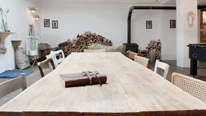 Un comedor espacioso con una gran mesa de madera, paredes blancas y una araña.