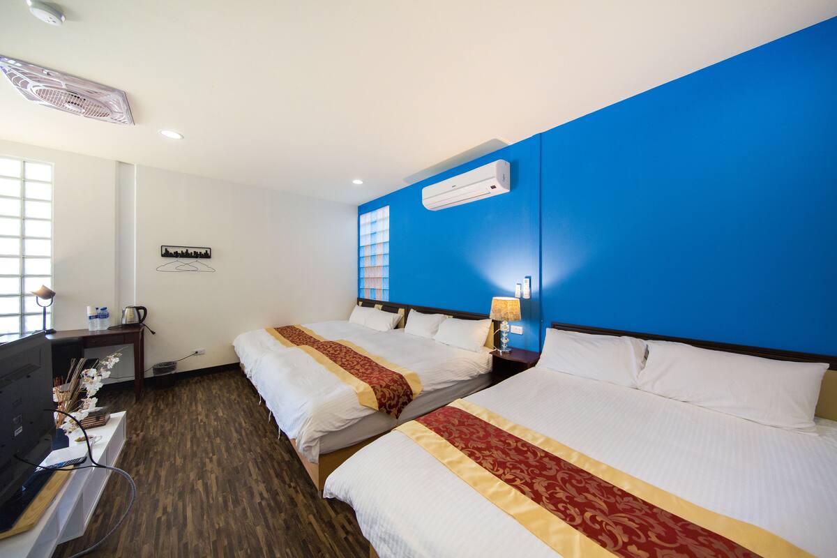 Ein Hotelzimmer mit zwei Betten, einem Schreibtisch, einem Stuhl, einem Fernseher und einem Fenster.