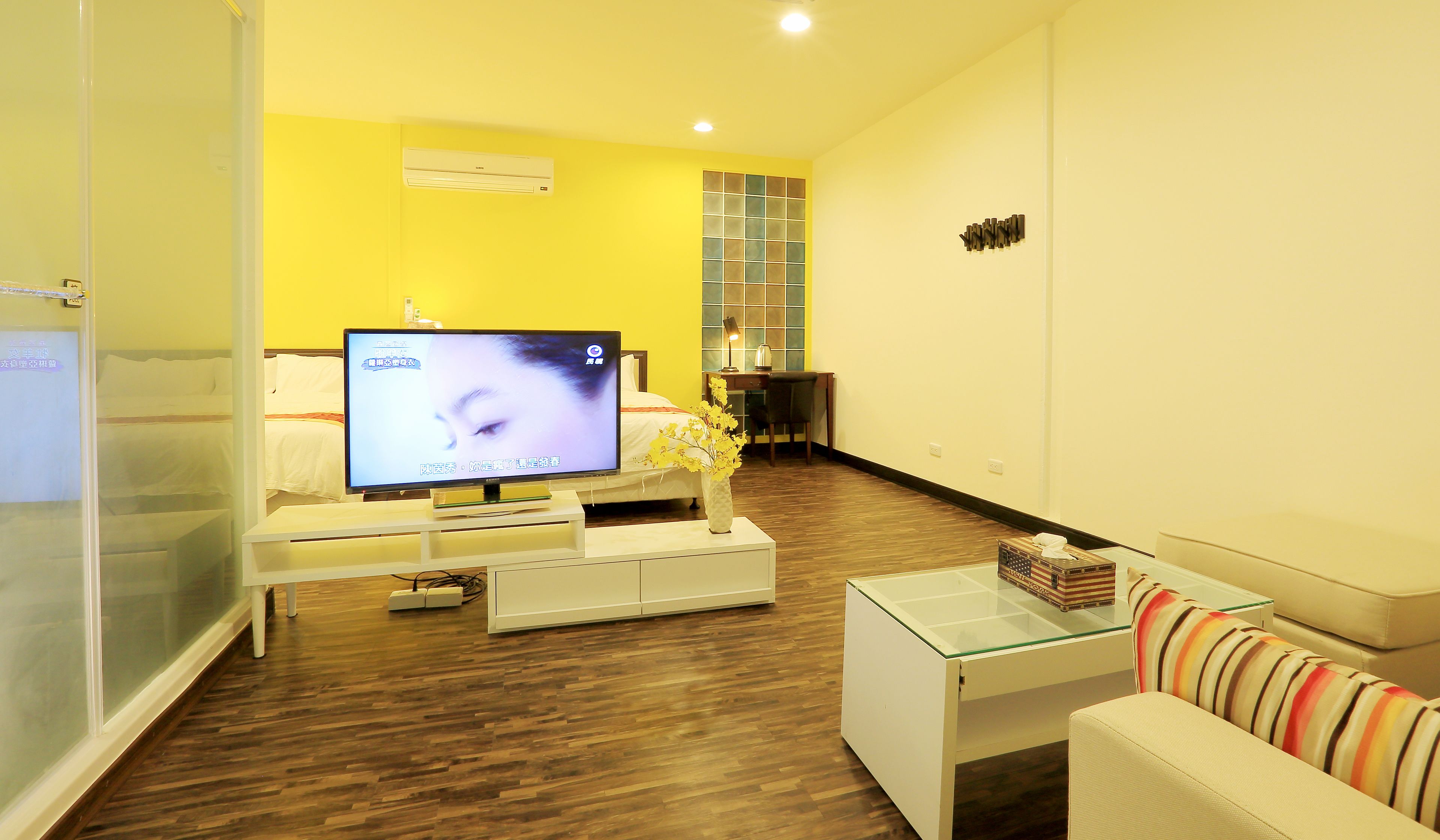 A modern living room with a flat-screen TV, a glass coffee table, a sofa, and a desk with a chair.