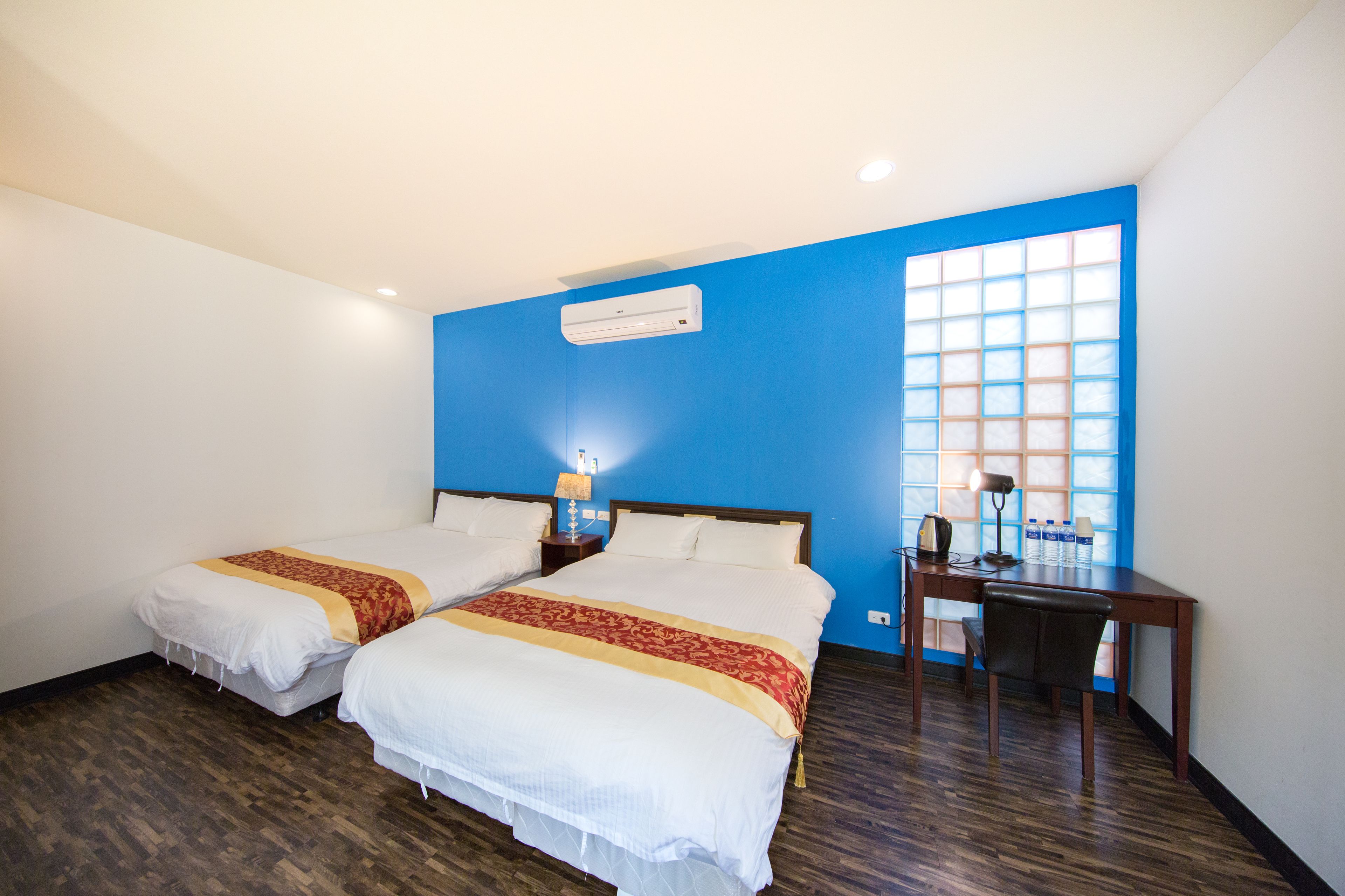 Habitación de hotel con dos camas, un escritorio y ventana con pared azul y vistas.