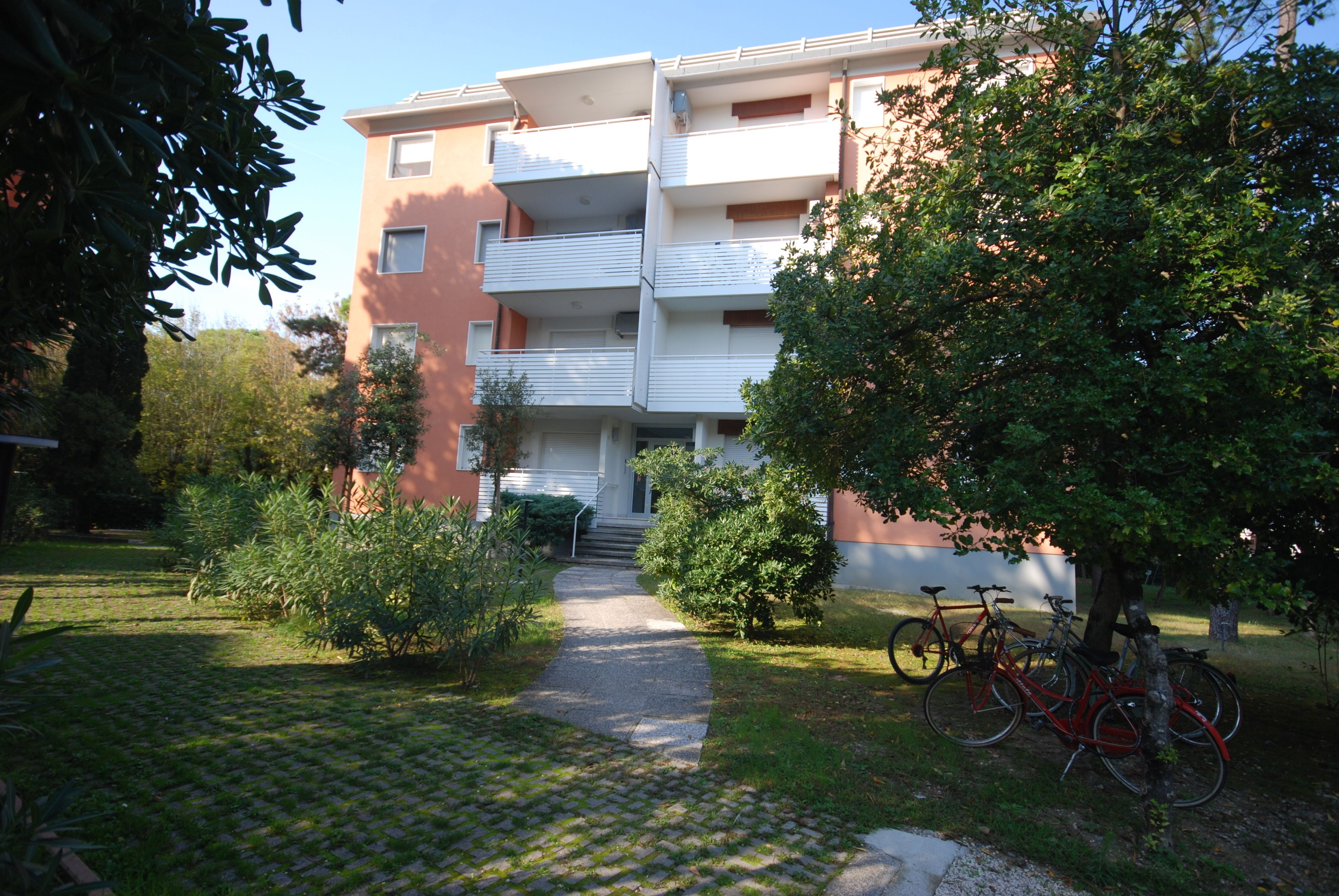 Un immeuble résidentiel à plusieurs étages, doté de balcons, avec un chemin pavé menant à l’entrée et des vélos garés à l’extérieur.