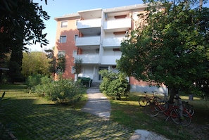 A multi-story residential building with balconies, a paved pathway leading to the entrance, and bicycles parked outside. - Valgardena (Lignano Sabbiadoro)