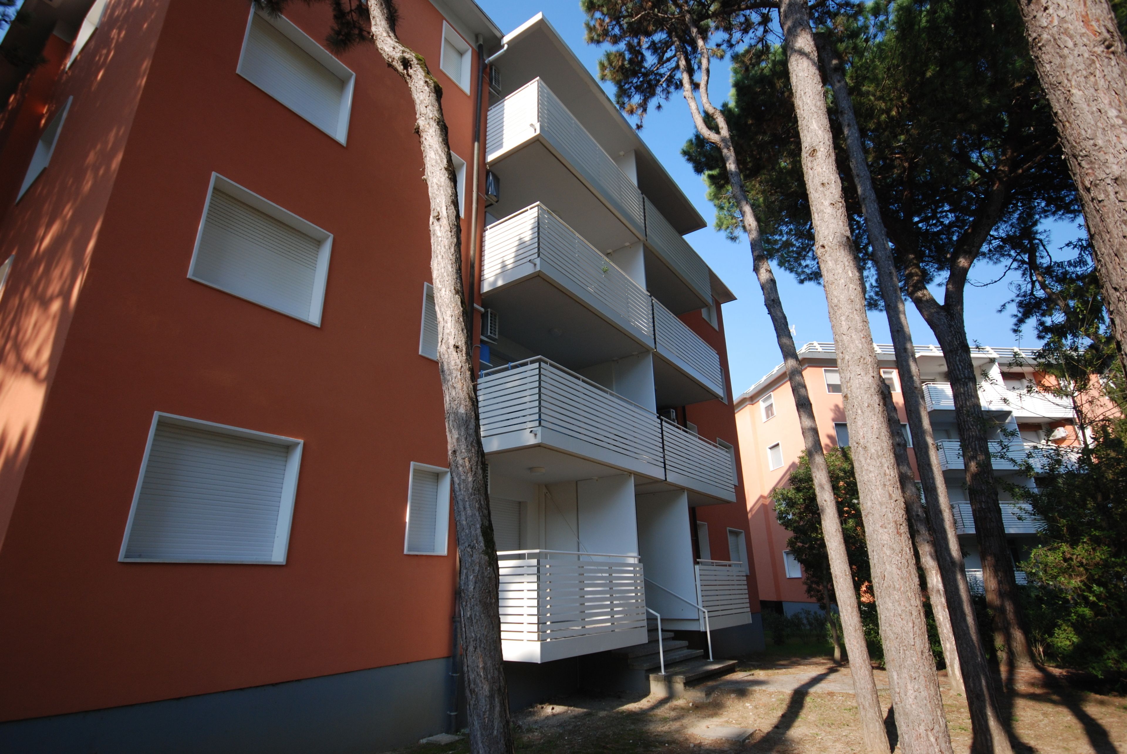 Un edificio residencial de varios pisos con balcones, fachada roja y árboles circundantes.