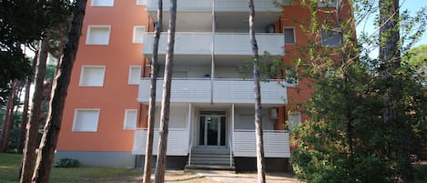 A multi-story building with balconies, surrounded by trees and a grassy area.