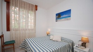 Une chambre à coucher comprenant un lit, une chaise, une table de chevet, une lampe et un tableau représentant une scène de plage.
