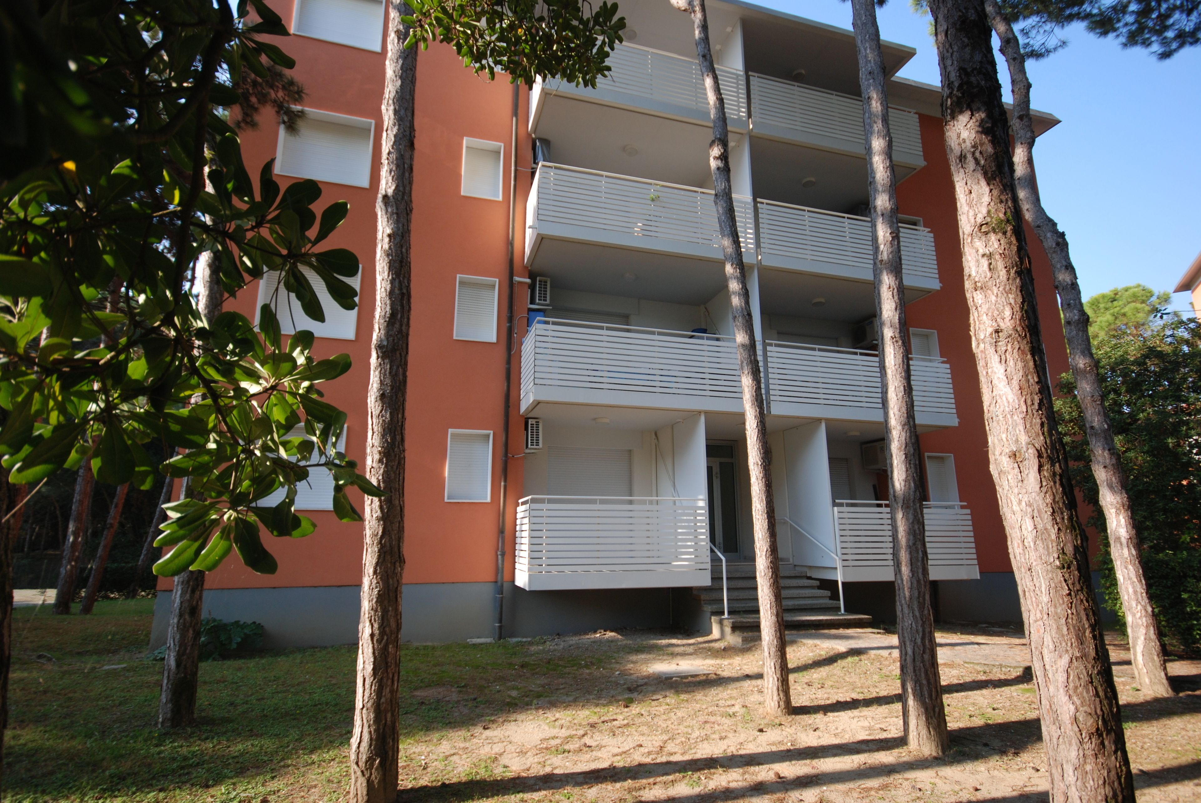 Un edifici d'apartaments de diverses plantes amb balcons, envoltat d'arbres.