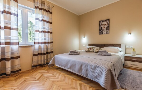 Ein Hotelzimmer mit Bett, Nachttisch, Wandleuchte und einem Fenster mit Vorhängen.