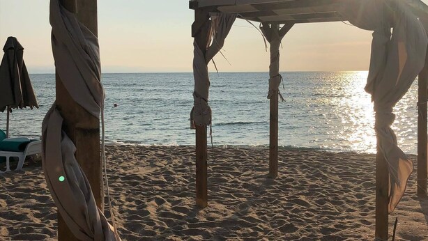 A beach scene with a wooden structure, possibly a beach chair or small table, and a beach umbrella in the background. - Sunny Suites by Casa Del Mare (Varna)