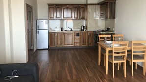 A compact kitchen with wooden cabinets, a white refrigerator, and a dining area with wooden chairs and a table. - Sunny Suites by Casa Del Mare (Varna)