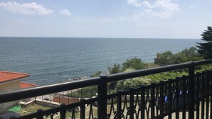 A balcony with a view of the sea, a fenced garden area, and a building with a red roof. - Sunny Suites by Casa Del Mare (Varna)