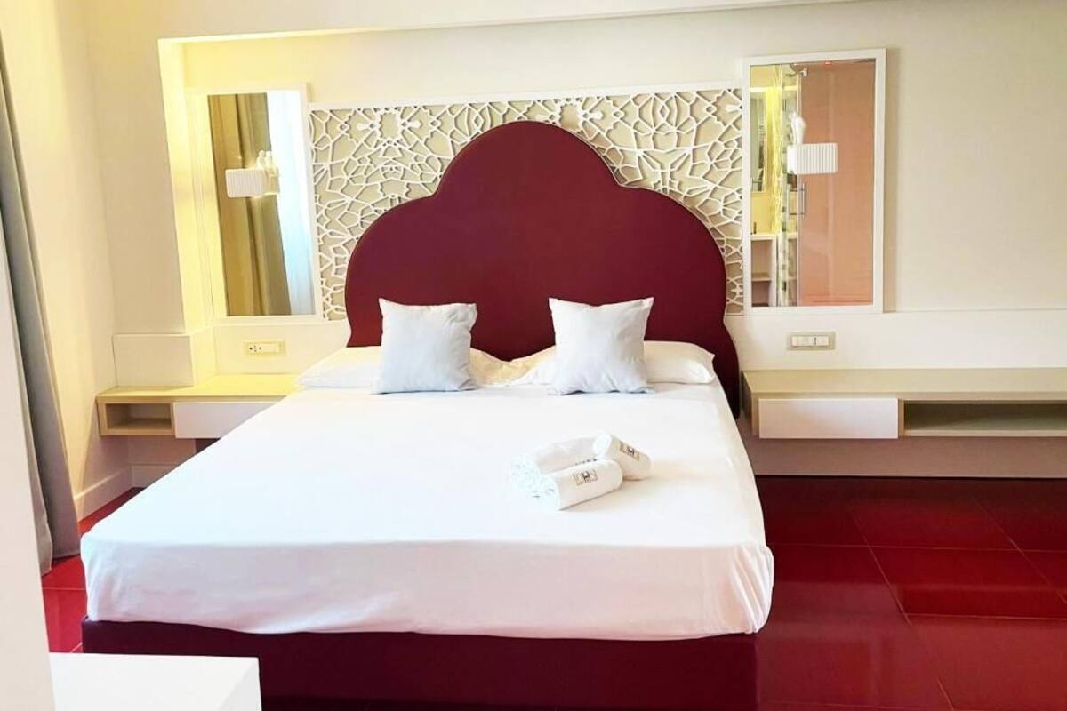 A hotel room with a large bed, white bedding, a red headboard, and a decorative wall panel.