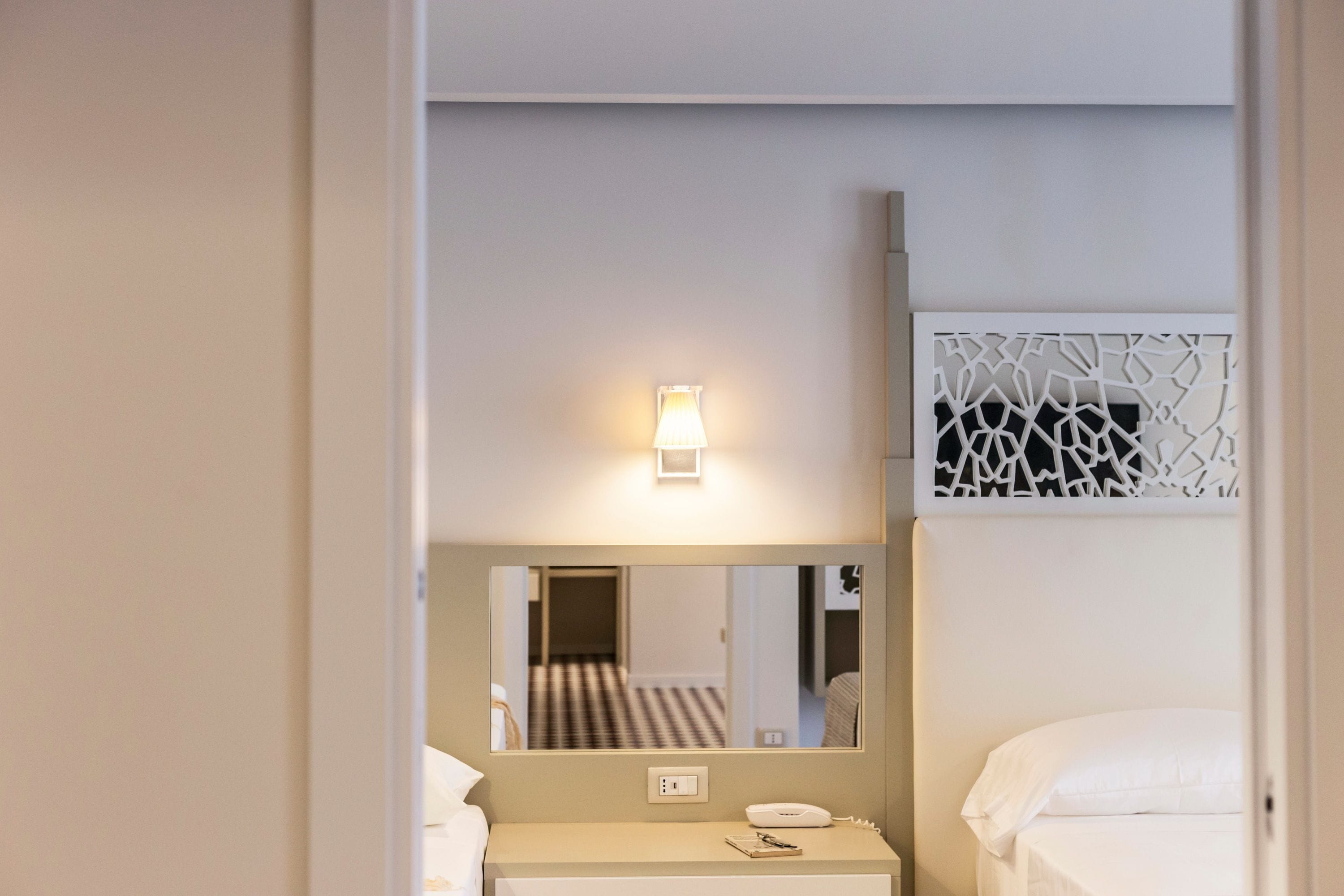 Quarto de hotel com cama, mesa de cabeceira, luminária e um painel decorativo na parede.