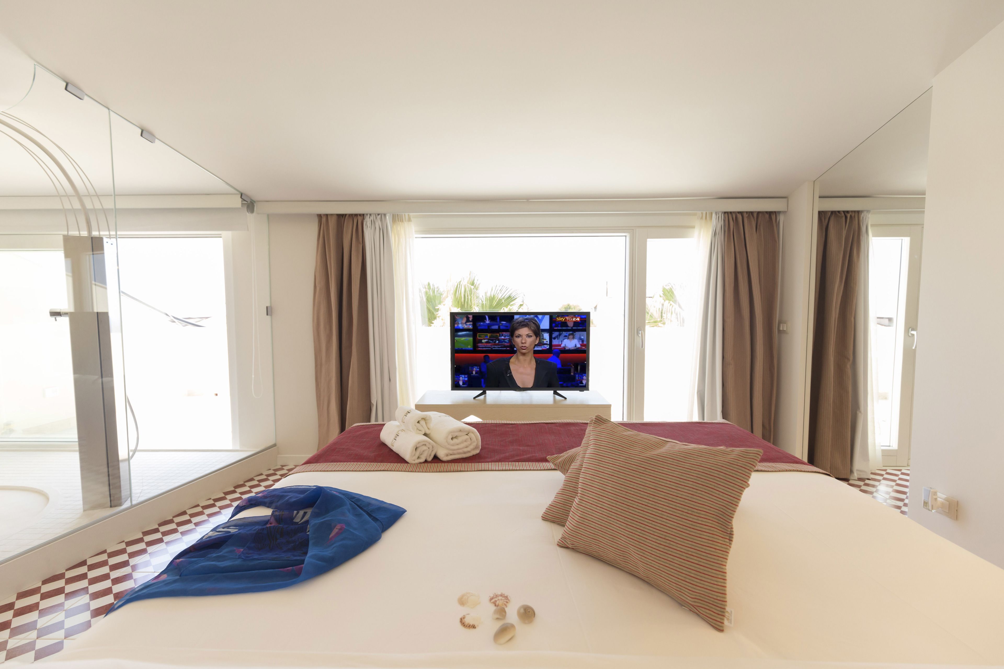 Habitación de hotel con una cama grande, televisión y vistas a palmeras.