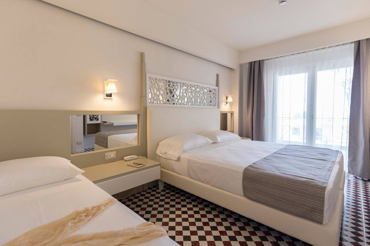 A hotel room with a large bed, a bedside table with a lamp, a mirror, and a check-in counter.