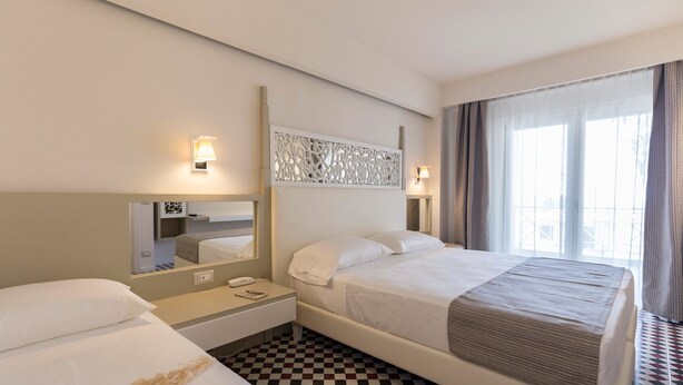 Une chambre d’hôtel avec un grand lit, une table de chevet avec une lampe, un miroir et un comptoir d’enregistrement.